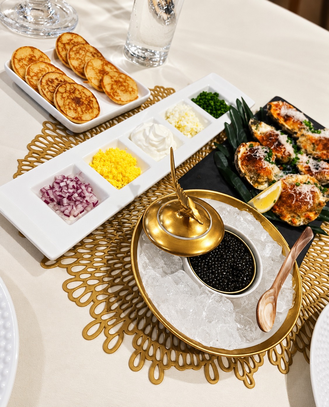 Caviar on ice with blini, traditional accompaniments and baked shellfish on a white and gold dining table